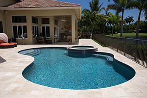 Kidney shaped pools are extremely popular and this one features bench seating tucked into a gentle curve by the raised spillover spa. The StoneScapes Aqua Blue finish by NPT has a Touch of Glass which makes it sparkle in the sun.