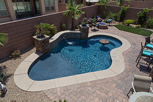 Have a small backyard? Consider adding a freeform pool like this! This backyard is full of features with a corner fire pit, in pool seating area, outdoor dining table, and grill bar.