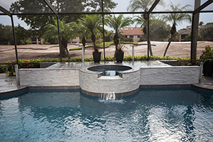 The centerpiece of this screened pool is the raised wall and spillover spa with white ledger stone. The contrasting NPT Magnetite waterline tile adds a bold stripe that ties in perfectly with the decking and coping.