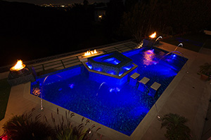 Heavy tile application elevates the drama of this geometric, tile-finish swimming pool, enveloping every available surface from the in-pool spa to the fire pots and island pads. The theatrical results make  California poolscape a preferred gathering spot for the night.