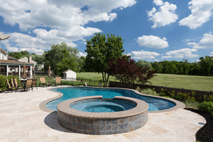 Great pool designs complement your home and environment, like this freeform pool and curvaceous travertine deck that mirror the clouds above, finished in NPT's ColorScapes Bora Bora Blue.