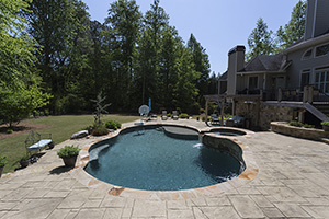 This Georgia home is packed with people-pleasing amenities like a raised deck with sheer descents over the deep end of the pool, an attached spill-over spa, a large sun shelf, a pergola with cozy seating and a basketball goal. NPT StoneScapes Tahoe Blue pool finish provides the elegant green-blue watercolor.