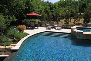 This pool features a vanishing edge tiled with NPT's Verona Boticas Green, perfectly complimenting the StoneScapes Tahoe Blue finish with added teal accent stone. Light-colored travertine deck contrasts beautifully with the poolscape.