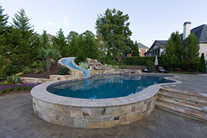 Local stone coping and stamp concrete decking surround this freeform poolscape in natural beauty. Further enhancing the organic feel is the green-blue NPT StoneScapes Tropics Blue pool finish and verdant landscaping.