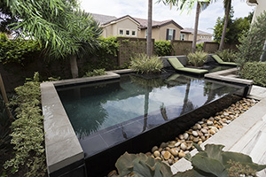 This incredible geometric poolscape defines contemporary natural style with its infinity edge spilling over into a bed of river rocks, lush landscaping and earth-tone decor.