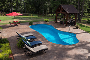 Enhance the area around your fiberglass pool with hardscapes. This homeowner selected decorative concrete to suit their rustic woodland-inspired backyard.