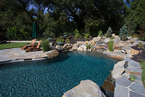 Like a secret garden carved from the forest, this California poolscape provides instant tranquility with its towering trees, natural stone accents, and soothing blue waters, courtesy of NPT StoneScapes Midnight Blue pool finish.