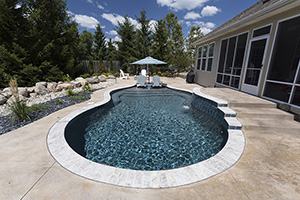 Opulent dark blue-green water emanates from every curve of this freeform poolscape, enhanced by Silver Travertine coping. A tanning ledge with deck chairs and a beachy umbrella make this the perfect spot for enjoying sunny days.