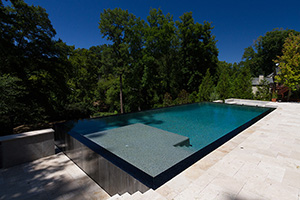 This Georgia homeowner opted for bold features when designing their backyard pool. The infinity edge runs the full length of the pool, spilling over into a lush tree-lined landscape. The pairing of NPT's StoneScapes ® Tropics Blue pool finish with AquaScapes Sapphire interlocking tile accentuates the clean lines of the pool and provides a striking variation to the light stone decking.