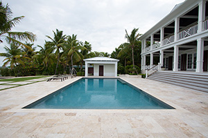 Enhance the vibrant beauty of your pool finish, like NPT StoneScapes Aqua Blue Mini Pebble pictured here, with light-colored accents. This homeowner selected a white pool house and travertine decking to create a soothing, elegant poolscape.