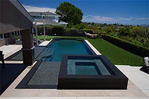 This rectangular pool features a raised attached spa with a perimeter overflow, surrounded by vibrant artificial turf and a putting green.