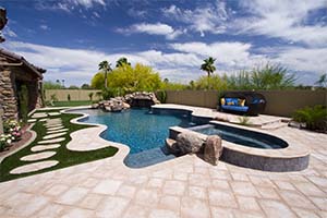 Tasteful custom pavers and stepping stones accent this lovely freeform pool that features a raised spa, grotto waterfall, and multiple tile mosaics.